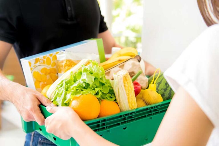 Delivery man delivering food to a woman at home - online grocery shopping service concept
